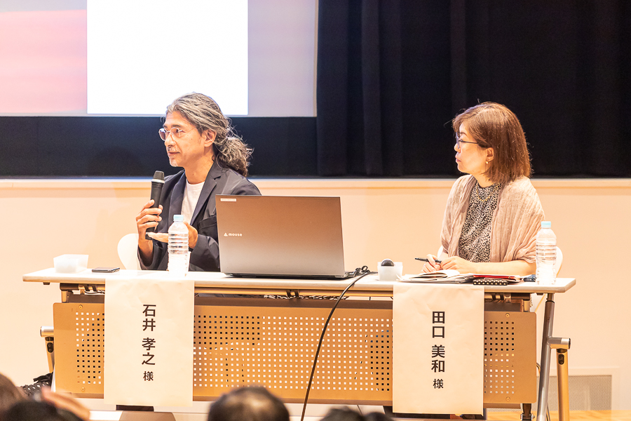 シンポジウム会場の壇上で話す2名の写真