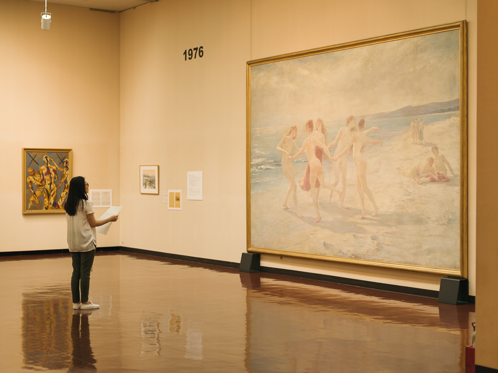 女性が紙を持ちながら壁にかかった大きな絵画を見ている写真